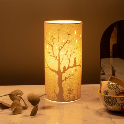 Image shows tube shaped beige fabric lamps with white Cat & Bird designs painted on and cut out shapes which a warm light shines out of.
