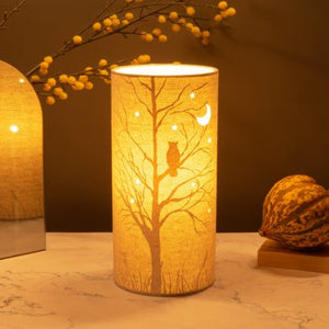 Image shows tube shaped beige fabric lamps with white Owl designs painted on and cut out shapes which a warm light shines out of.