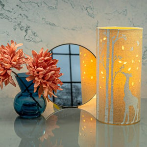 Image shows tube shaped beige fabric lamps with white Giraffe designs painted on and cut out shapes which a warm light shines out of.