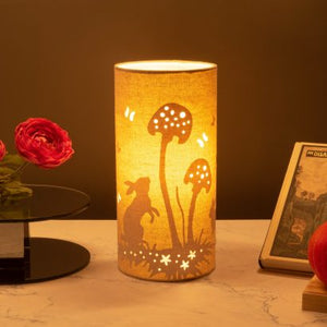 Image shows tube shaped beige fabric lamps with white Rabbit designs painted on and cut out shapes which a warm light shines out of.