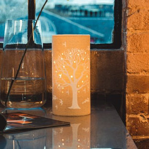 Image shows tube shaped beige fabric lamps with whiteTree of Life designs painted on and cut out shapes which a warm light shines out of.
