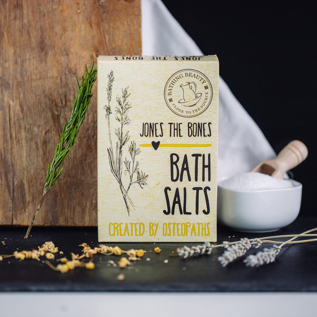 Image displays a picture of a yellow box, with floral illustrations and rustic style font which reads 'Jones The Bones - Bath Salts'.