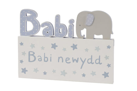 Image shows white plaque with wooden elephant and 'Babi newydd' inscription.