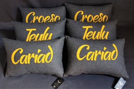 Woollen rectangle cushion in Slate Grey with 'Cariad' written on in yellow.
